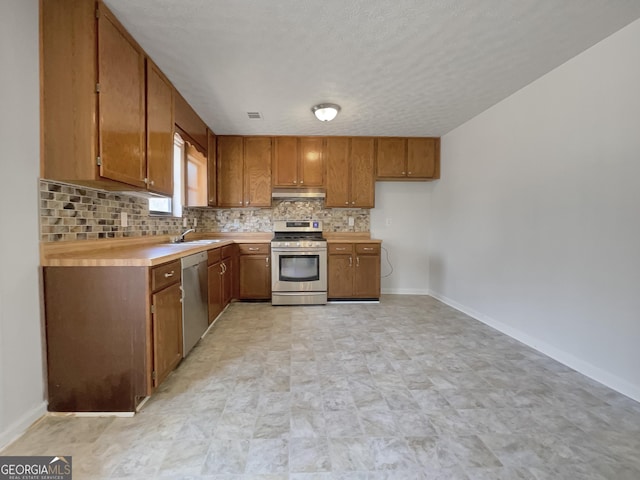 kitchen with under cabinet range hood, stainless steel appliances, brown cabinetry, and a sink