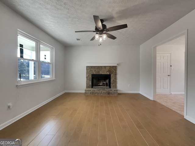 unfurnished living room with visible vents, baseboards, a stone fireplace, and wood finished floors