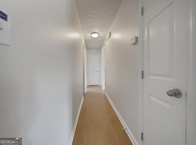 corridor featuring attic access, baseboards, and light wood finished floors