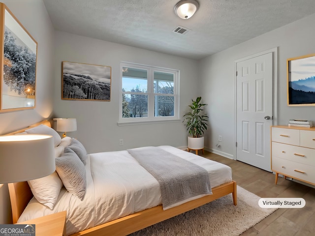 bedroom featuring visible vents, baseboards, a textured ceiling, and light wood-style flooring