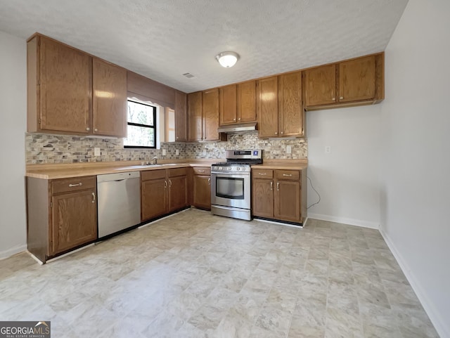 kitchen featuring stainless steel range with gas cooktop, light countertops, under cabinet range hood, dishwasher, and brown cabinets