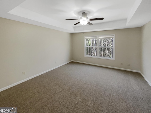 carpeted empty room featuring baseboards, a tray ceiling, and a ceiling fan