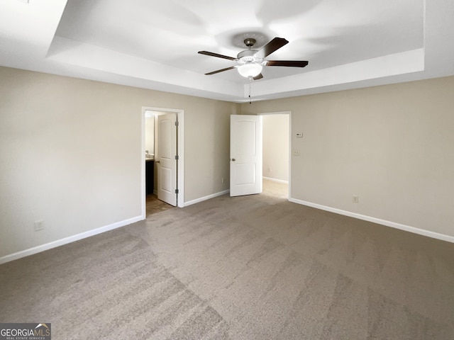 unfurnished bedroom featuring ceiling fan, baseboards, carpet flooring, ensuite bathroom, and a raised ceiling