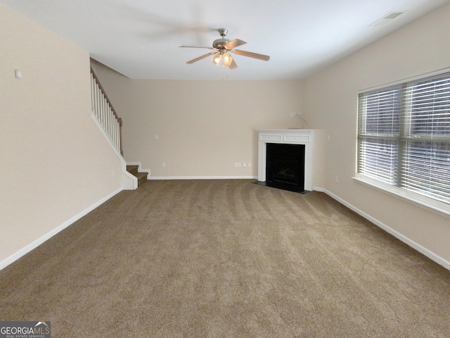 unfurnished living room with baseboards, carpet, a fireplace with flush hearth, stairs, and a ceiling fan