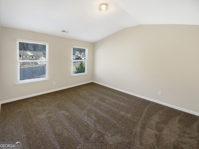 spare room with visible vents, baseboards, dark colored carpet, and vaulted ceiling