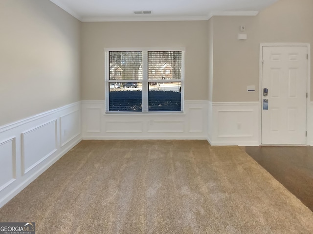 carpeted empty room featuring crown molding, a decorative wall, visible vents, and a wainscoted wall