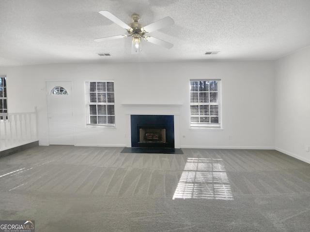 unfurnished living room with visible vents, a textured ceiling, a fireplace with flush hearth, and carpet floors