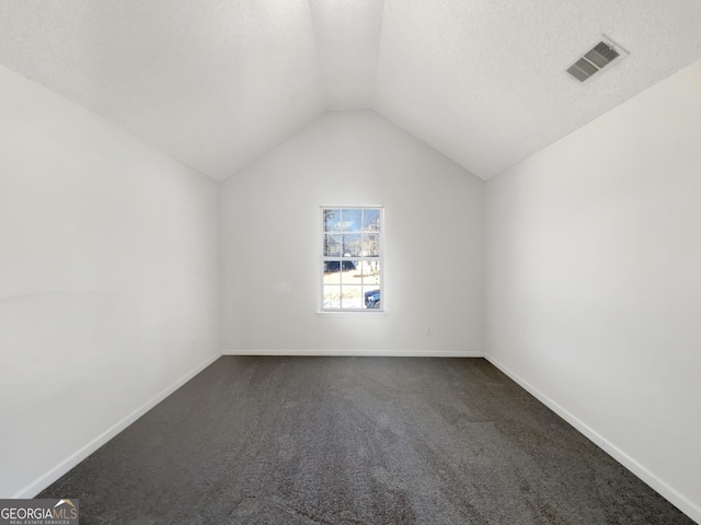 bonus room featuring visible vents, a textured ceiling, dark carpet, baseboards, and vaulted ceiling