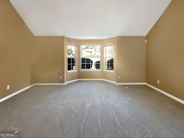 carpeted spare room with baseboards and vaulted ceiling