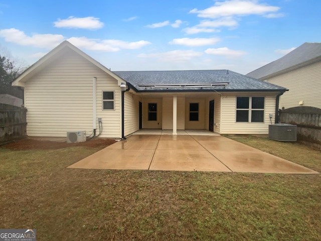 rear view of house with a shingled roof, fence, central AC, a lawn, and a patio area