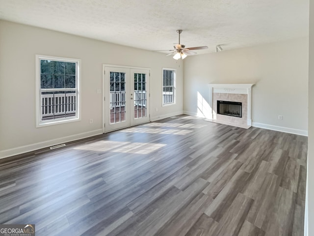 unfurnished living room with dark wood-type flooring, a tiled fireplace, a textured ceiling, french doors, and baseboards