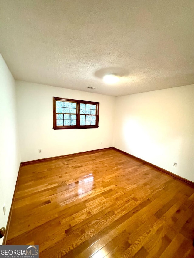 spare room featuring wood finished floors, baseboards, and a textured ceiling