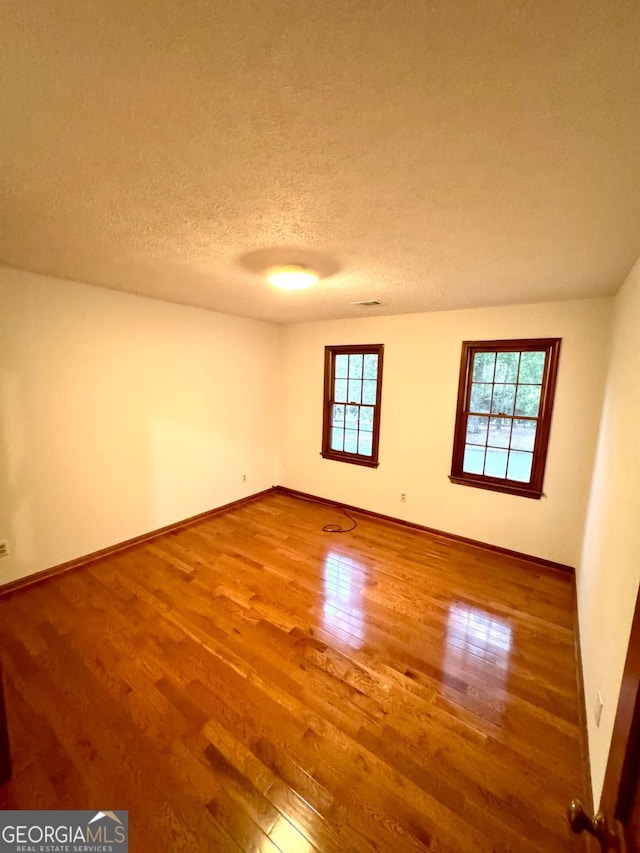 empty room featuring wood finished floors, baseboards, and a textured ceiling