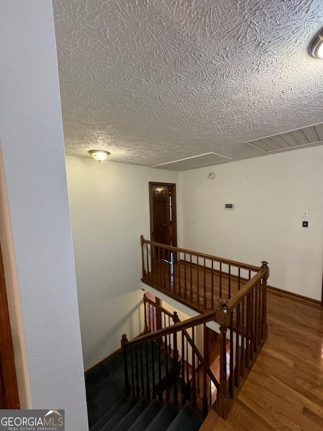 staircase featuring visible vents, baseboards, attic access, wood finished floors, and a textured ceiling