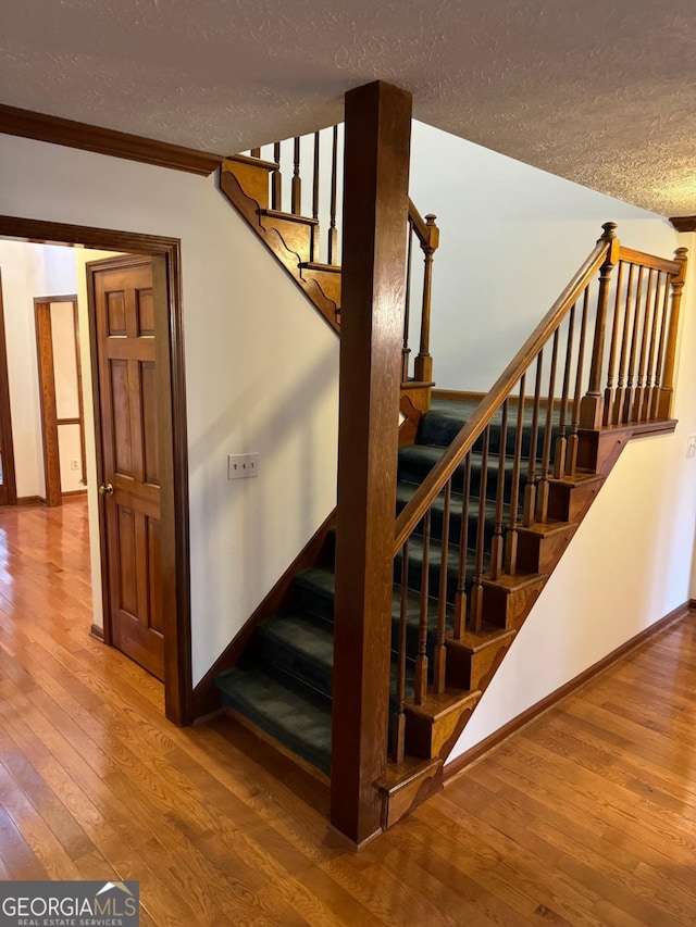 stairway with a textured ceiling, baseboards, and hardwood / wood-style flooring