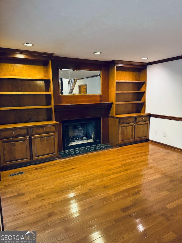 unfurnished living room with wood finished floors, visible vents, baseboards, a fireplace, and crown molding