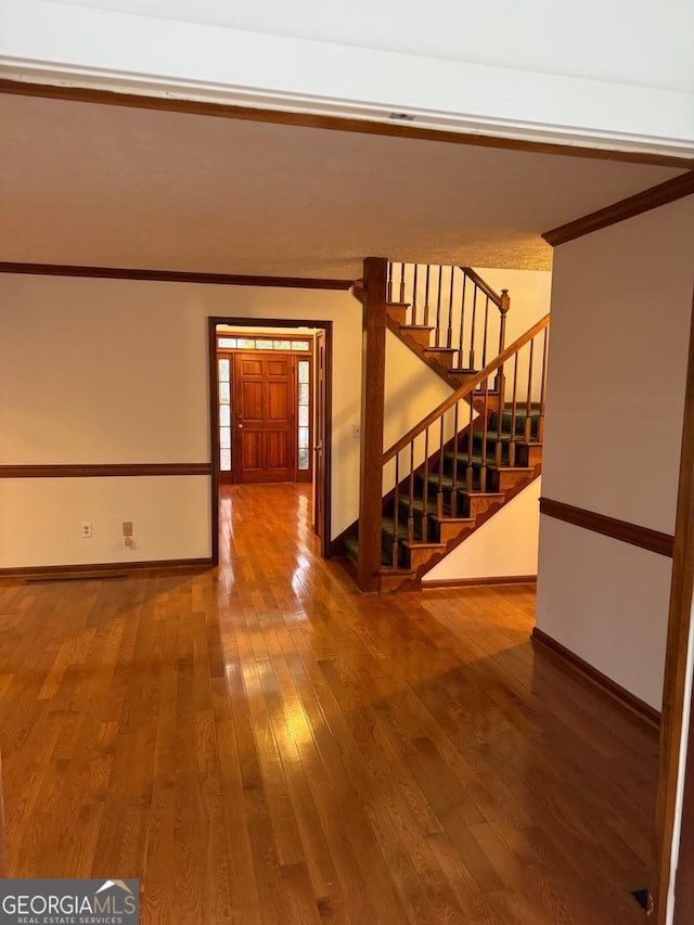 empty room with stairs, hardwood / wood-style flooring, crown molding, and baseboards