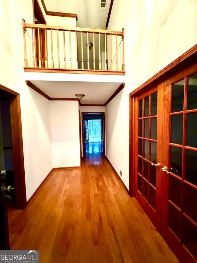 hallway with wood finished floors, visible vents, baseboards, a high ceiling, and ornamental molding