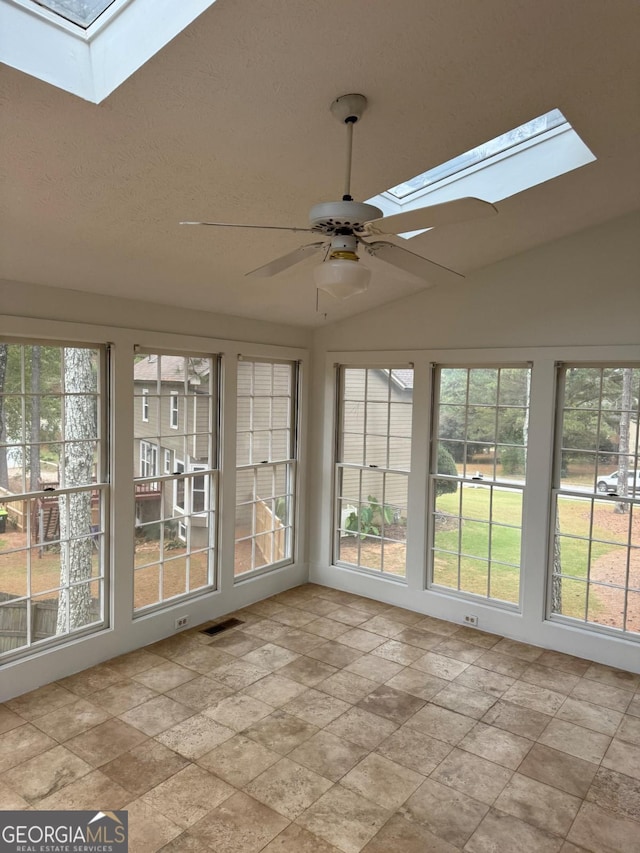 unfurnished sunroom featuring a wealth of natural light, visible vents, vaulted ceiling with skylight, and ceiling fan