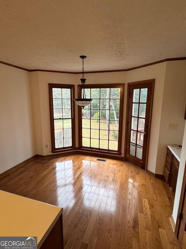 unfurnished dining area featuring light wood finished floors, visible vents, baseboards, ornamental molding, and a textured ceiling