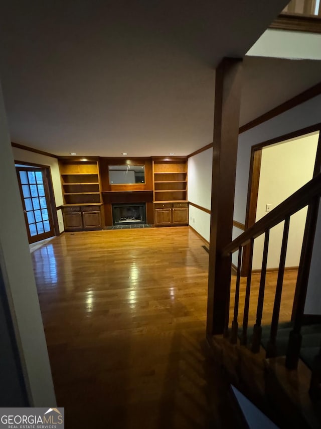 living area with built in shelves, stairs, ornamental molding, a fireplace, and wood finished floors