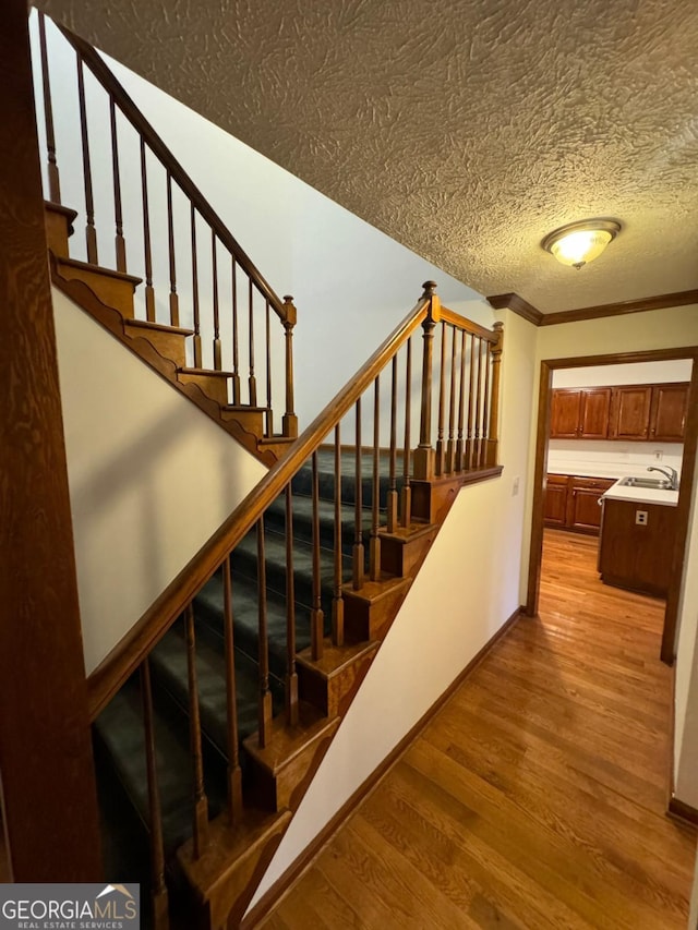 stairs featuring a textured ceiling, crown molding, baseboards, and wood finished floors