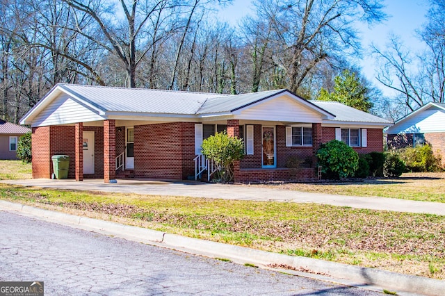 single story home featuring a carport, brick siding, driveway, and metal roof