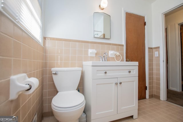 half bath featuring a wainscoted wall, toilet, tile walls, and vanity