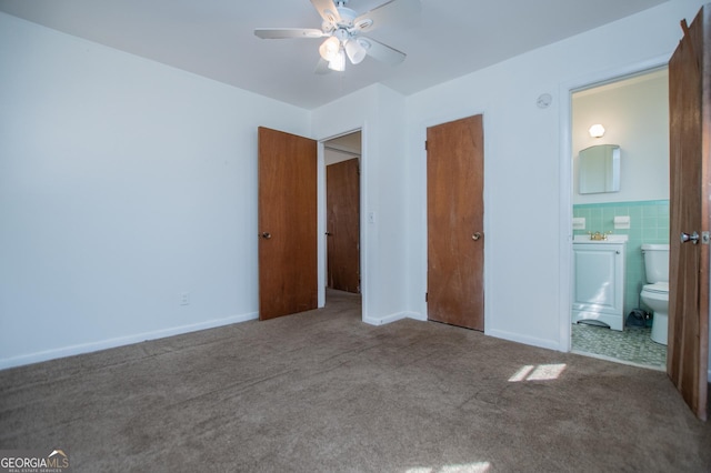 unfurnished bedroom with connected bathroom, tile walls, a ceiling fan, and carpet floors