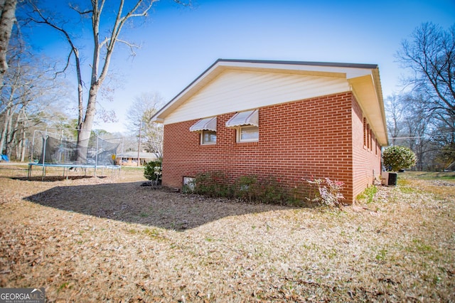 view of home's exterior with a trampoline, central AC, and brick siding