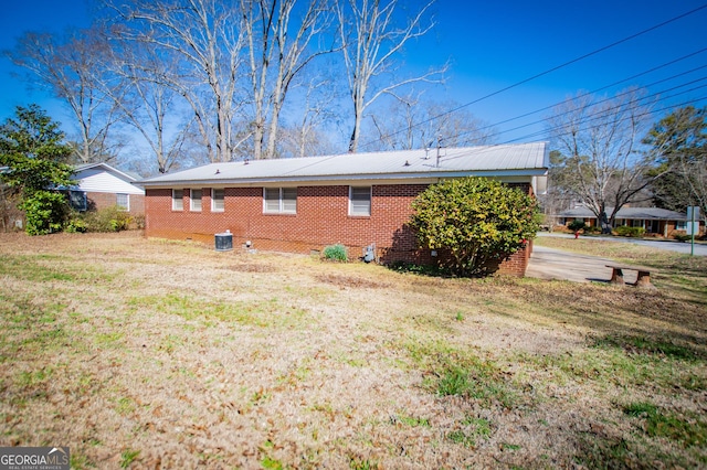 rear view of house with brick siding, a lawn, metal roof, and central AC