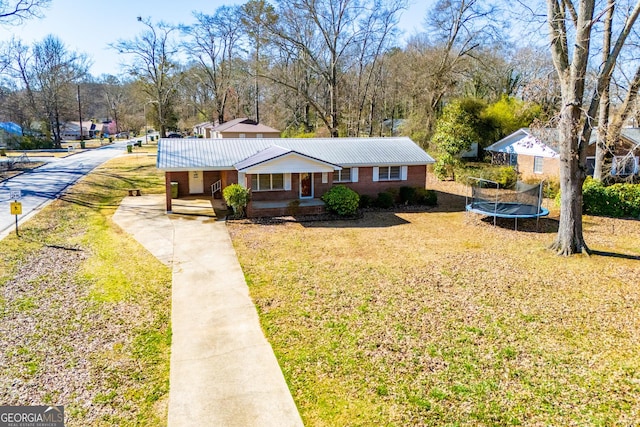 view of front of home featuring brick siding, metal roof, a trampoline, and a front yard