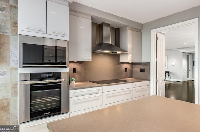 kitchen featuring light countertops, white cabinetry, wall chimney range hood, black electric cooktop, and backsplash