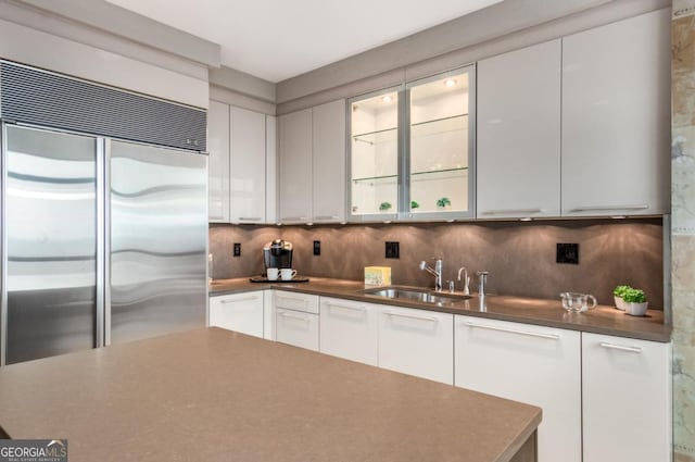 kitchen featuring backsplash, white cabinets, stainless steel built in fridge, and a sink