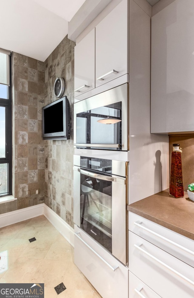 kitchen featuring light tile patterned floors, white cabinets, baseboards, and stainless steel oven