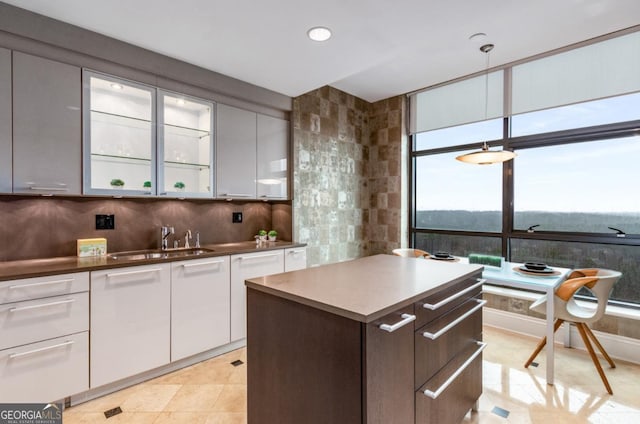 kitchen with a kitchen island, a sink, glass insert cabinets, white cabinetry, and backsplash