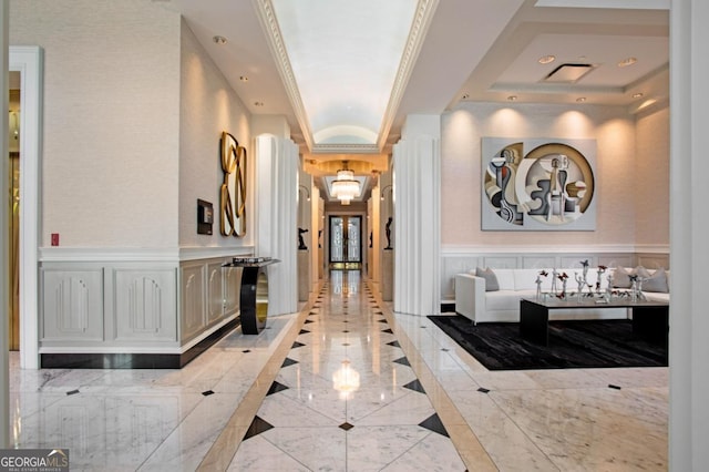 hall with a decorative wall, a wainscoted wall, marble finish floor, and a raised ceiling