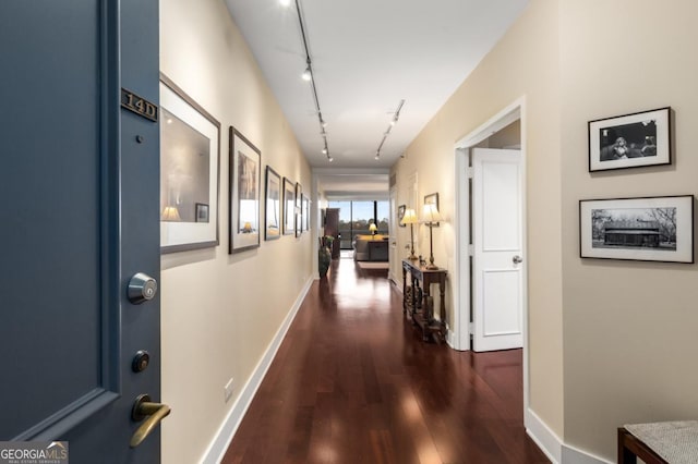 hall with baseboards, track lighting, and dark wood-style flooring