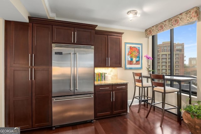 kitchen with built in refrigerator, ornamental molding, light stone counters, dark wood-style floors, and decorative backsplash