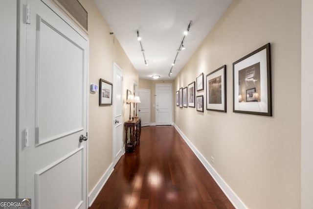 corridor featuring rail lighting, baseboards, and dark wood-style flooring