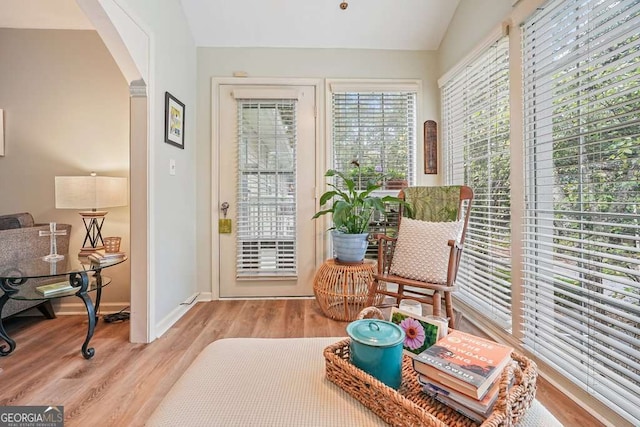 living area featuring arched walkways, vaulted ceiling, baseboards, and wood finished floors