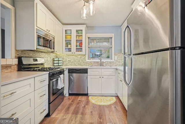 kitchen with a sink, stainless steel appliances, light countertops, glass insert cabinets, and light wood-type flooring