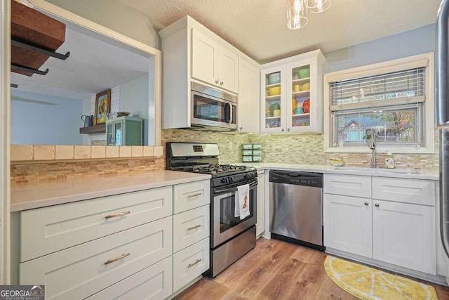 kitchen with tasteful backsplash, glass insert cabinets, light countertops, appliances with stainless steel finishes, and light wood-style floors