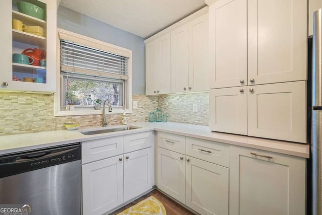 kitchen featuring a sink, light countertops, glass insert cabinets, stainless steel dishwasher, and backsplash