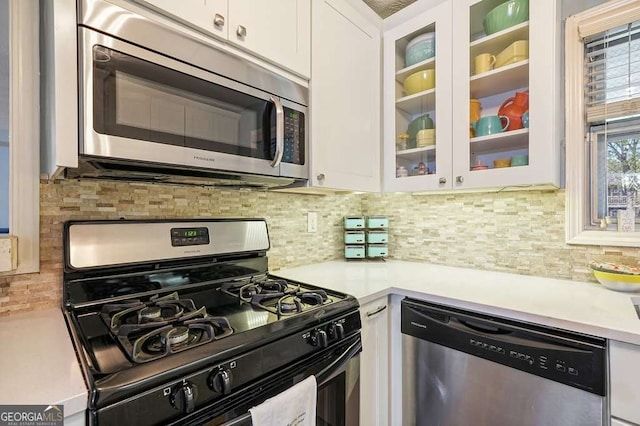 kitchen with stainless steel appliances, light countertops, glass insert cabinets, white cabinetry, and tasteful backsplash