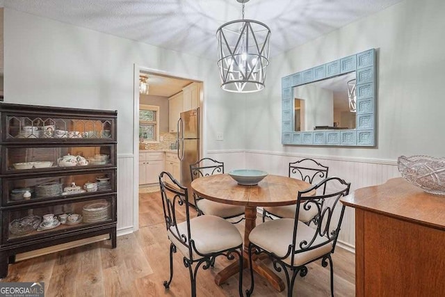 dining space featuring a wainscoted wall, a textured ceiling, light wood-type flooring, and a chandelier