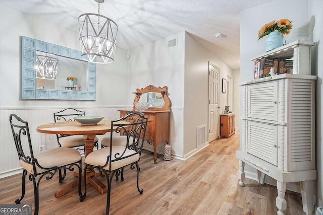 dining space with a wainscoted wall, visible vents, light wood finished floors, and a chandelier