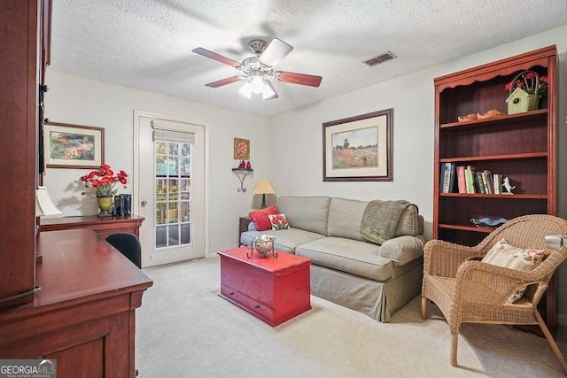 living area with visible vents, light colored carpet, a textured ceiling, and a ceiling fan