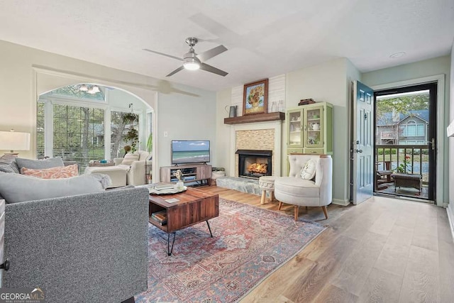 living area featuring light wood-type flooring, ceiling fan, and a fireplace