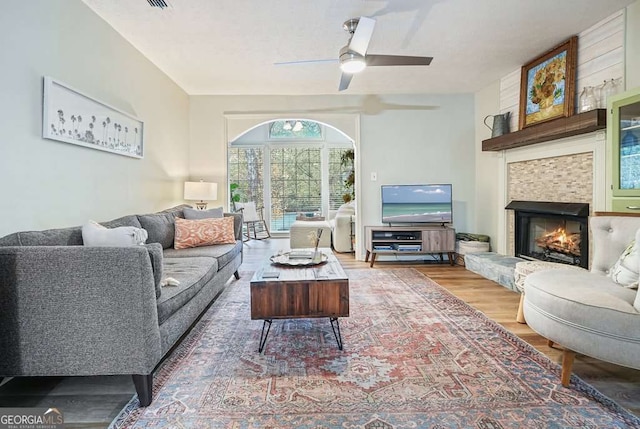 living room with wood finished floors, a ceiling fan, and a tile fireplace